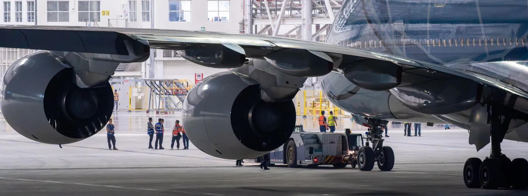 Wide-body aircraft under tow in a maintenance hangar, engineers in high-visibility vests beside the engines